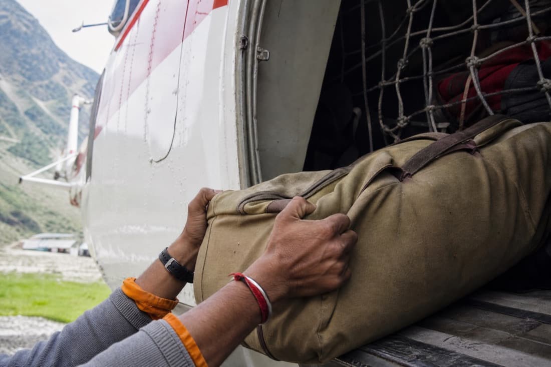 Hands loading a bag into a helicopter cargo bay